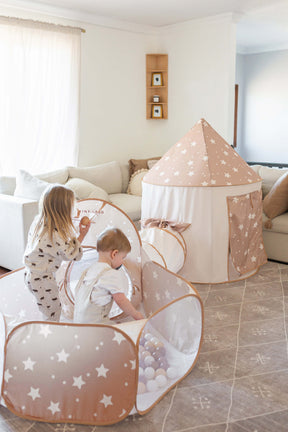 Two young children play in the Tiny Land® Compact Adventure 3-in-1 Play Tunnel, a star-patterned tent set up in a bright living room with a beige couch and sheer curtains.|brown