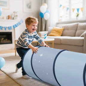 A smiling young boy in a striped shirt pushes the Tiny Land® Adventure Play Tunnel - Blue by Tiny Land, decorated with stars, in a bright living room filled with blue birthday balloons and banners.|blue