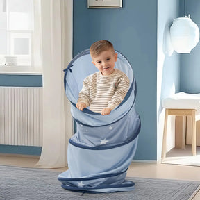 A smiling young boy stands inside the Tiny Land® Adventure Play Tunnel - Blue by Tiny Land, decorated with star patterns, in a bright room with light blue walls and a white radiator.|blue