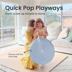 A smiling woman in a yellow dress hugs a young girl indoors as they hold the blue Tiny Land® Adventure Play Tunnel bag. Text reads: Quick Pop Playways—swift setup, easy storage, and includes the carry bag by Tiny Land.|blue