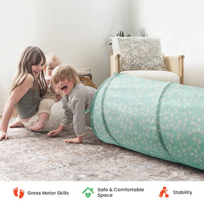 Three young children play and crawl through the Tiny Land® Adventure Play Tunnel, a light blue floral tunnel designed by Tiny Land, in a cozy, softly lit living room featuring a beige armchair and cushions in the background. Icons below highlight motor skills development, safety, and stability.|Green