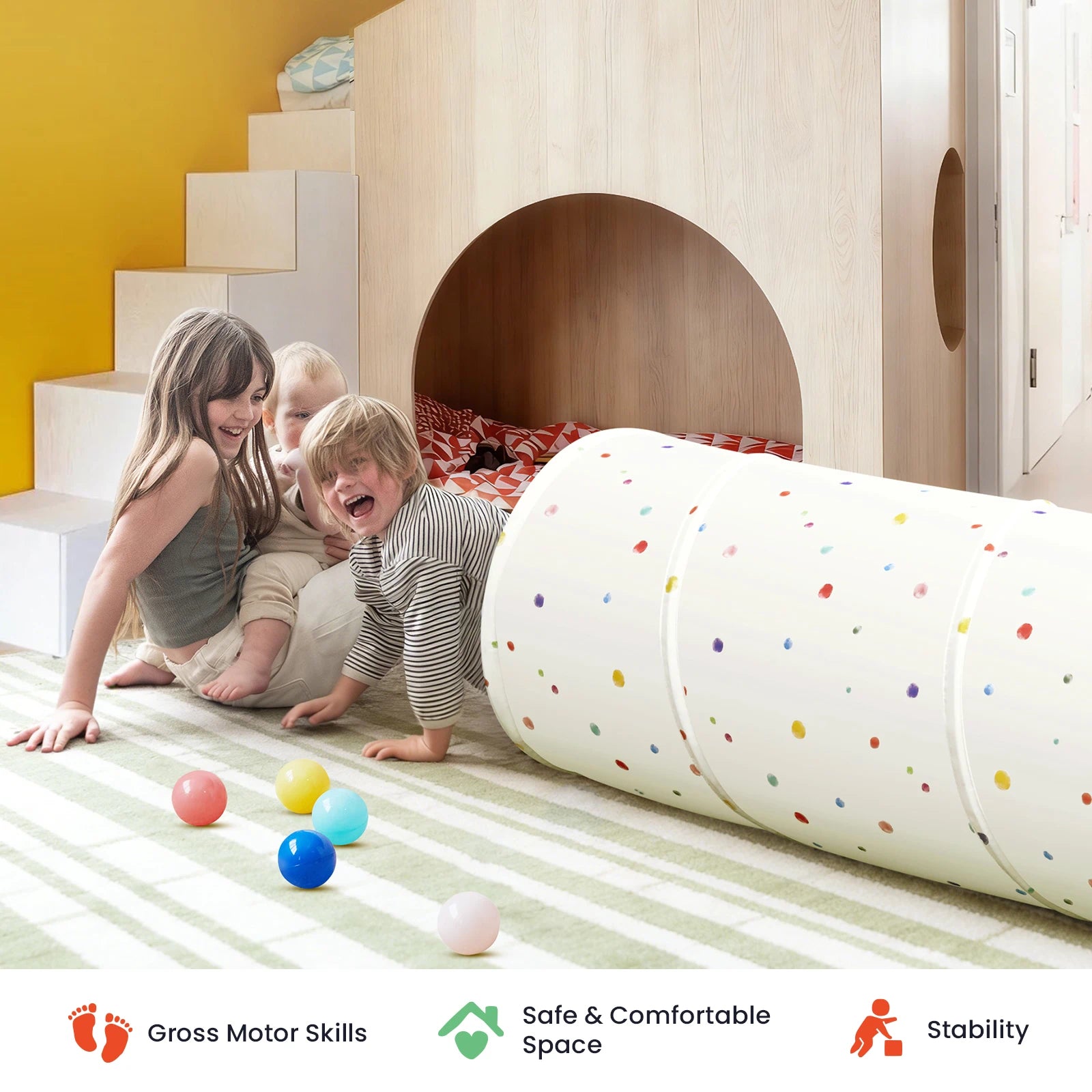 Two young children play on a striped rug in a cozy, modern playroom featuring the Tiny Land® Adventure Play Tunnel by Tiny Land, a wooden loft bed, and colorful balls. Three icons below highlight motor skills, safety, and stability.|Colorful Dots