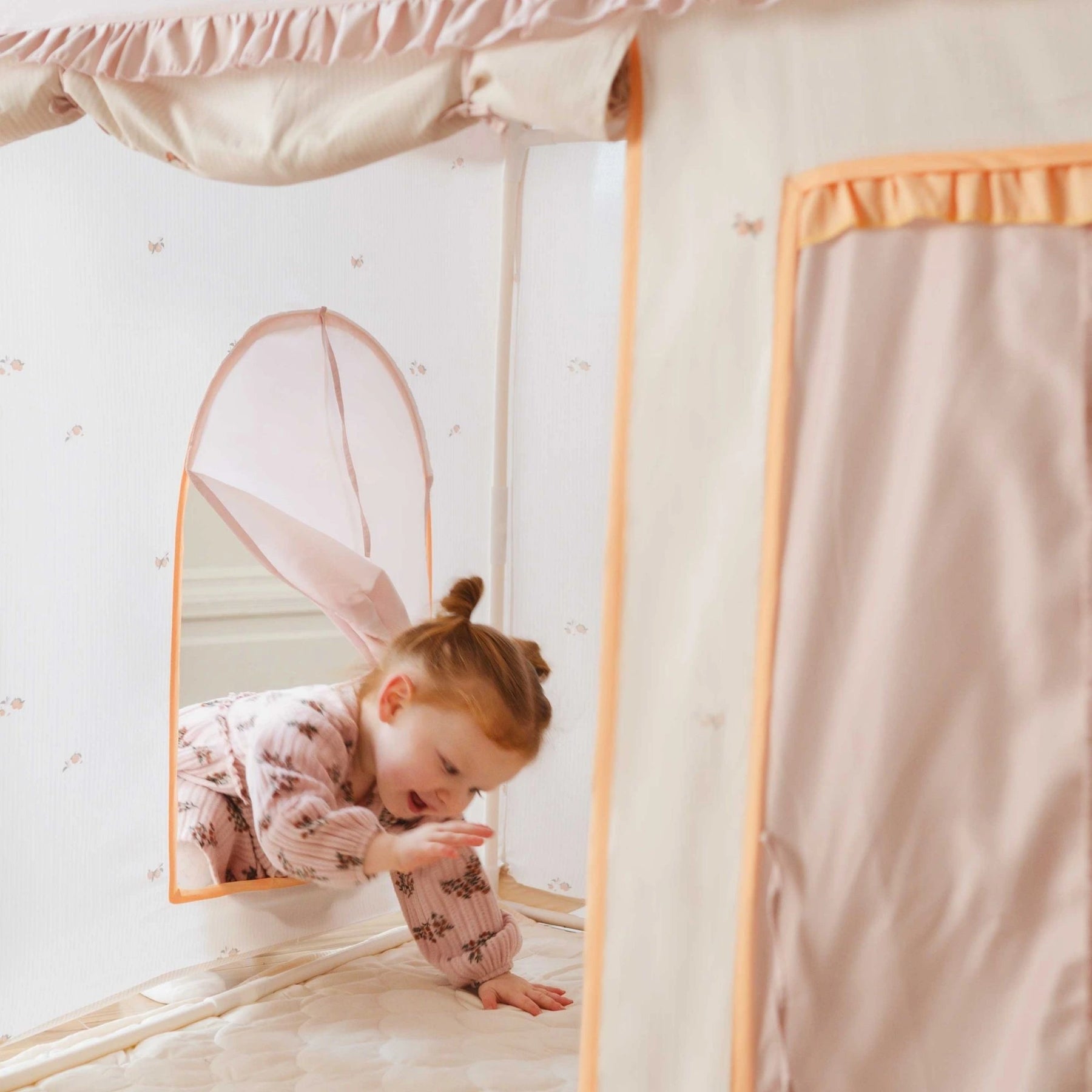A young child smiles and reaches out from a Tiny Land® Sweet Citrus Kids Play Tent by Tiny Land, a cozy white and pink indoor playhouse perfect for fun adventures on its soft padded floor.|pink