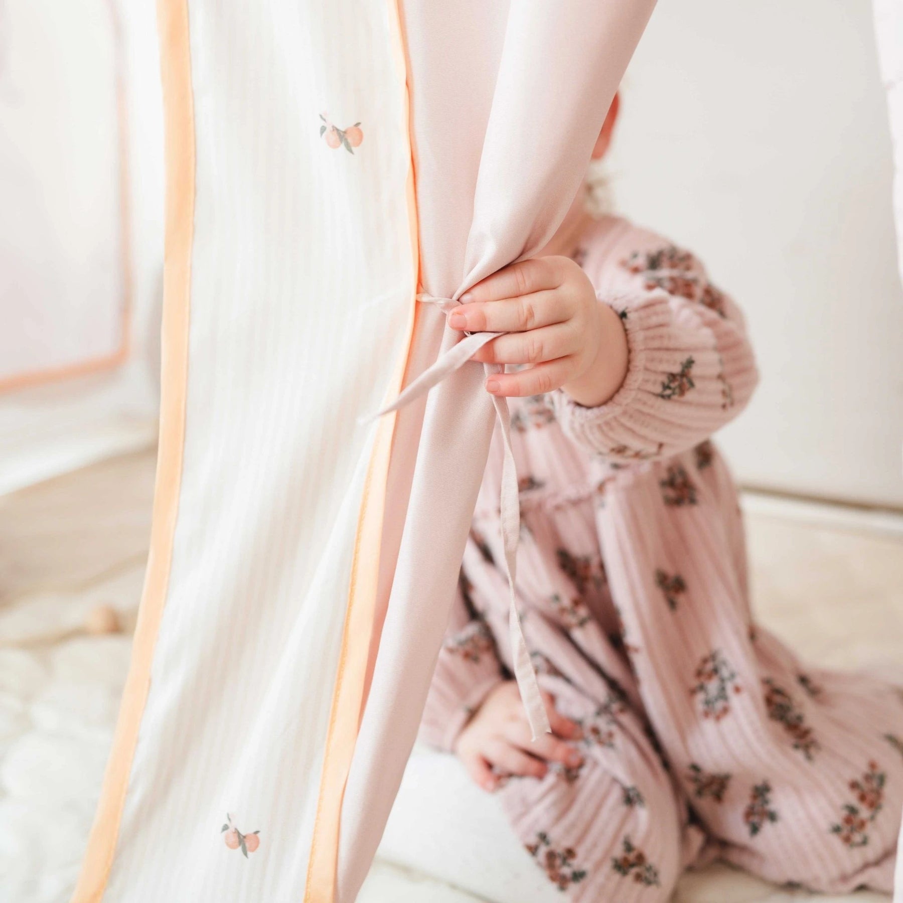 A young child, face hidden, playfully ties a soft curtain on the Tiny Land® Sweet Citrus Kids Play Tent – White and Pink Indoor Playhouse, creating a cozy indoor hideout that inspires imaginative play.|pink
