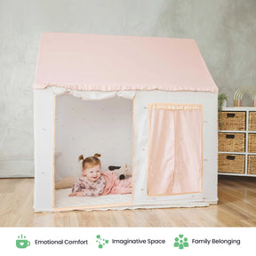 A young child smiles while sitting inside the Tiny Land® Playhouse Tent—a small, pink-and-white indoor tent for kids—set in a cozy room with wooden floors and storage baskets. Three icons and words are displayed below: Emotional Comfort, Imaginative Space, Family Belonging.|pink