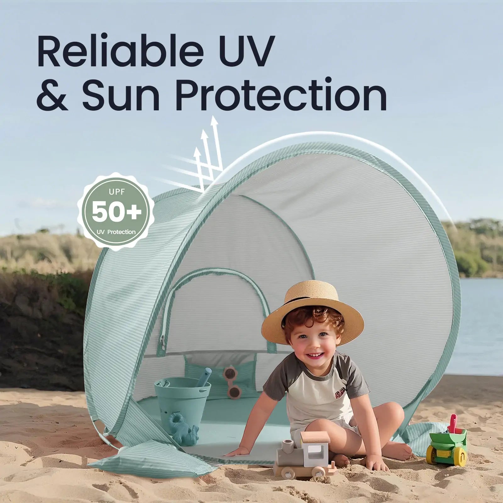A young child smiles inside the Tiny Land® Baby Beach Tent – Sea Blue by Tiny Land on a sandy beach, surrounded by toys. The open pop-up tent features illustrated sun rays and “Reliable UV & Sun Protection UPF 50+” text above.|Sea Blue