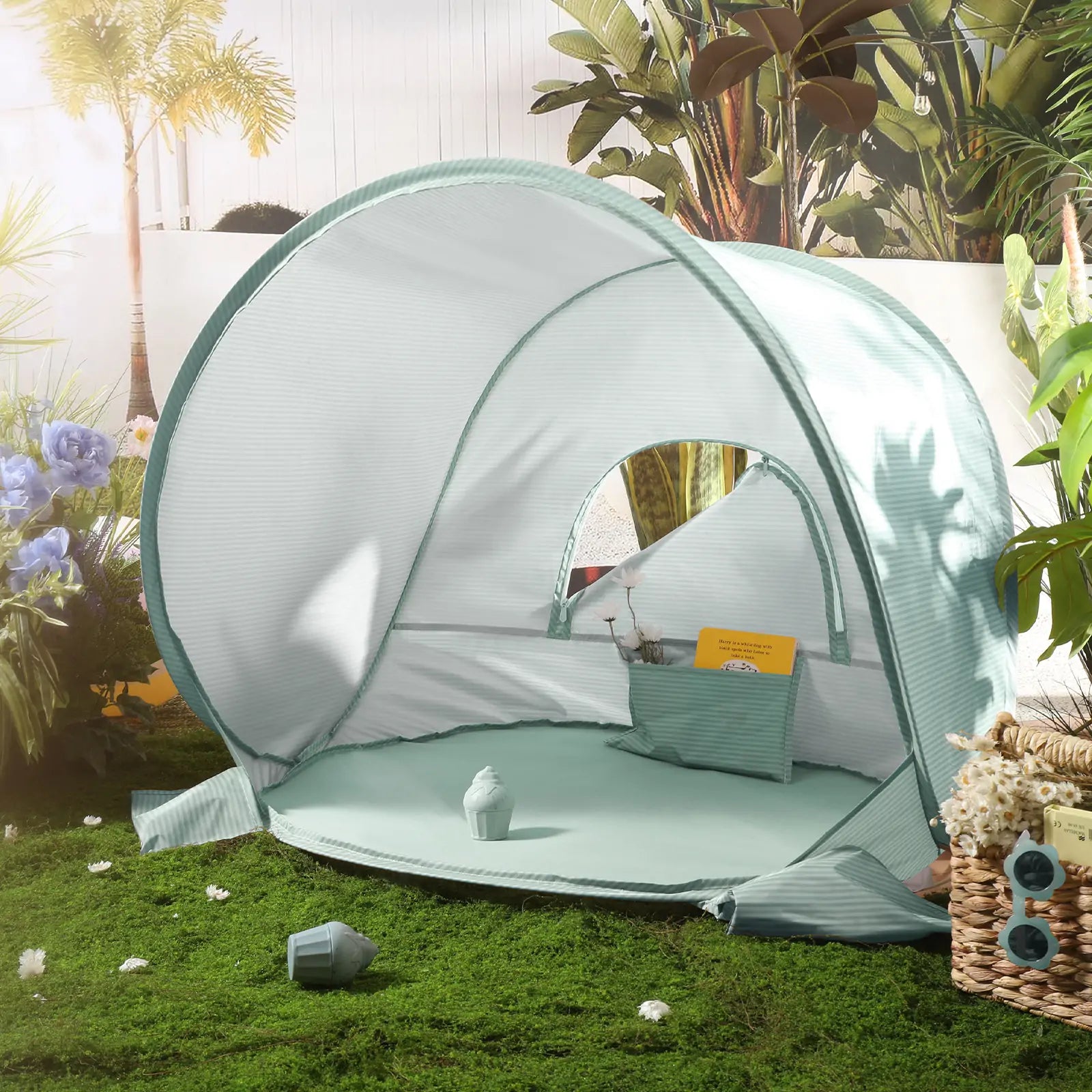 The Tiny Land® Baby Beach Tent – Sea Blue Play Tent for Outdoor Fun by Tiny Land sits on grass in a sunlit garden, featuring UV protection, a pillow, toys, and surrounded by plants, flowers, and a woven basket.|Sea Blue