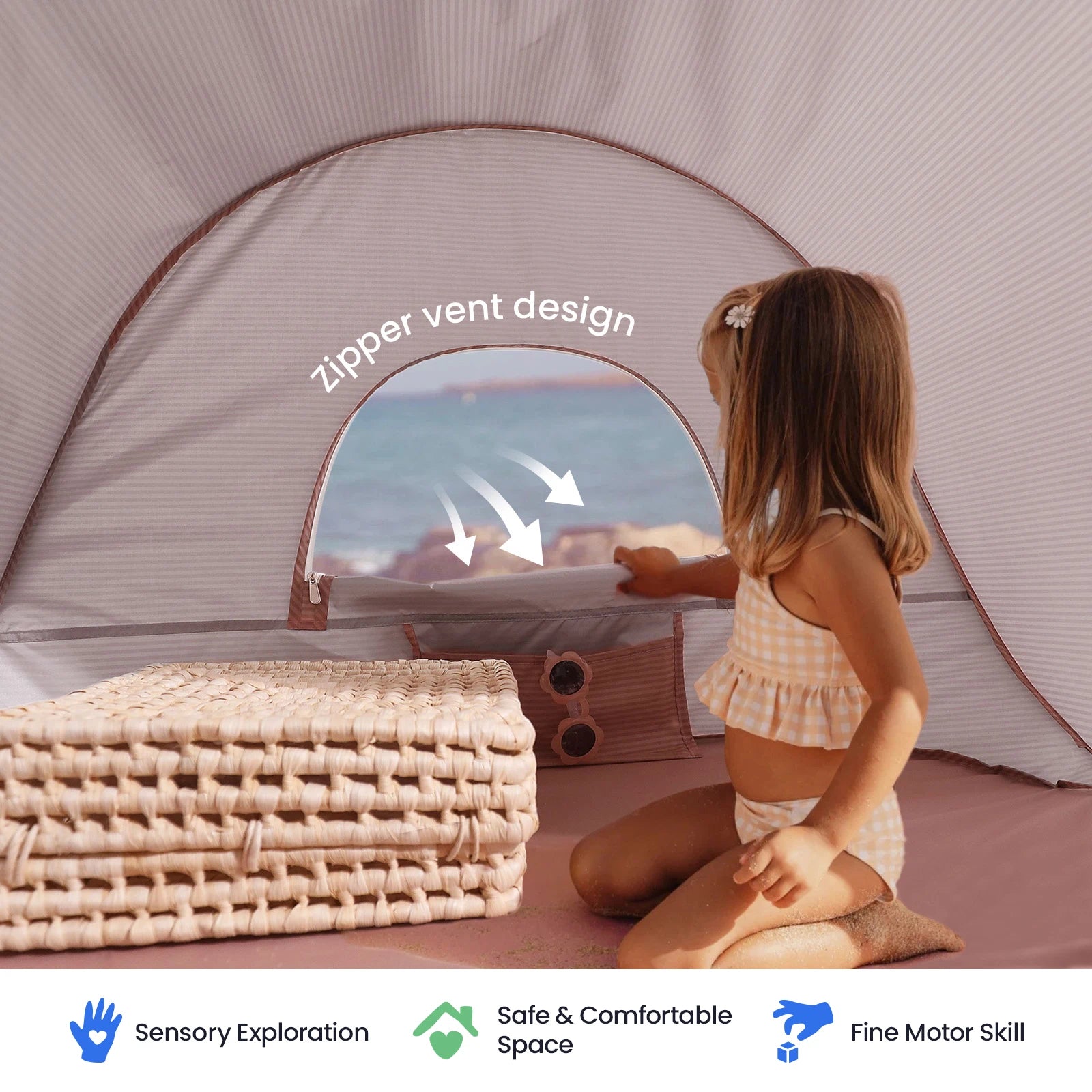 A young girl in a checkered swimsuit sits inside the Tiny Land® Baby Beach Tent – Play Tent for Outdoor Fun by Tiny Land, which features a convenient zipper vent and is set up near woven mats. This beach tent provides sensory exploration, a safe space, UV protection, and supports fine motor skill development.|Blush Pink