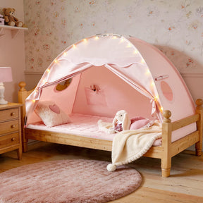 The Tiny Land® Versatile Kids Bed Tent & Play Tent by Tiny Land features a cozy wooden-framed children’s bed with a pink canopy, creating the perfect indoor tent for kids. It’s beautifully accented with fairy lights, a plush bunny, heart-shaped pillow, soft blanket, round rug, and floral wallpaper in a softly lit room.