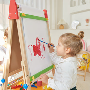A young girl with light brown hair in a ponytail paints with red on the Tiny Land® 3-in-1 Art Easel & Paper Roll Set by Tiny Land in a bright, cozy room, with art supplies scattered nearby.|red
