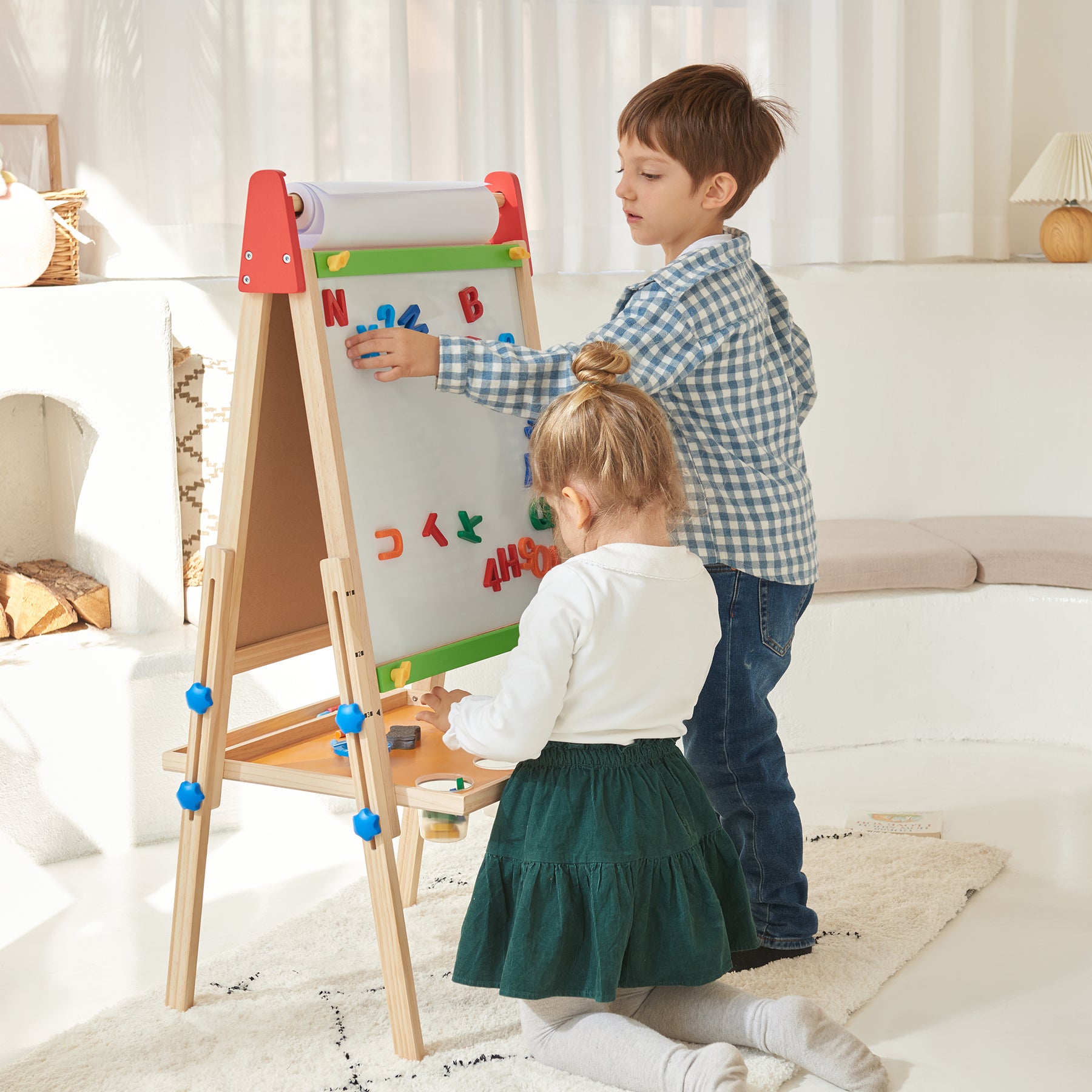 A young boy and girl play with colorful magnetic letters on the Tiny Land® 3-in-1 Art Easel for Kids in a bright, cozy room. The boy stands and reaches up while the girl kneels, both focused on arranging the magnets together.|red