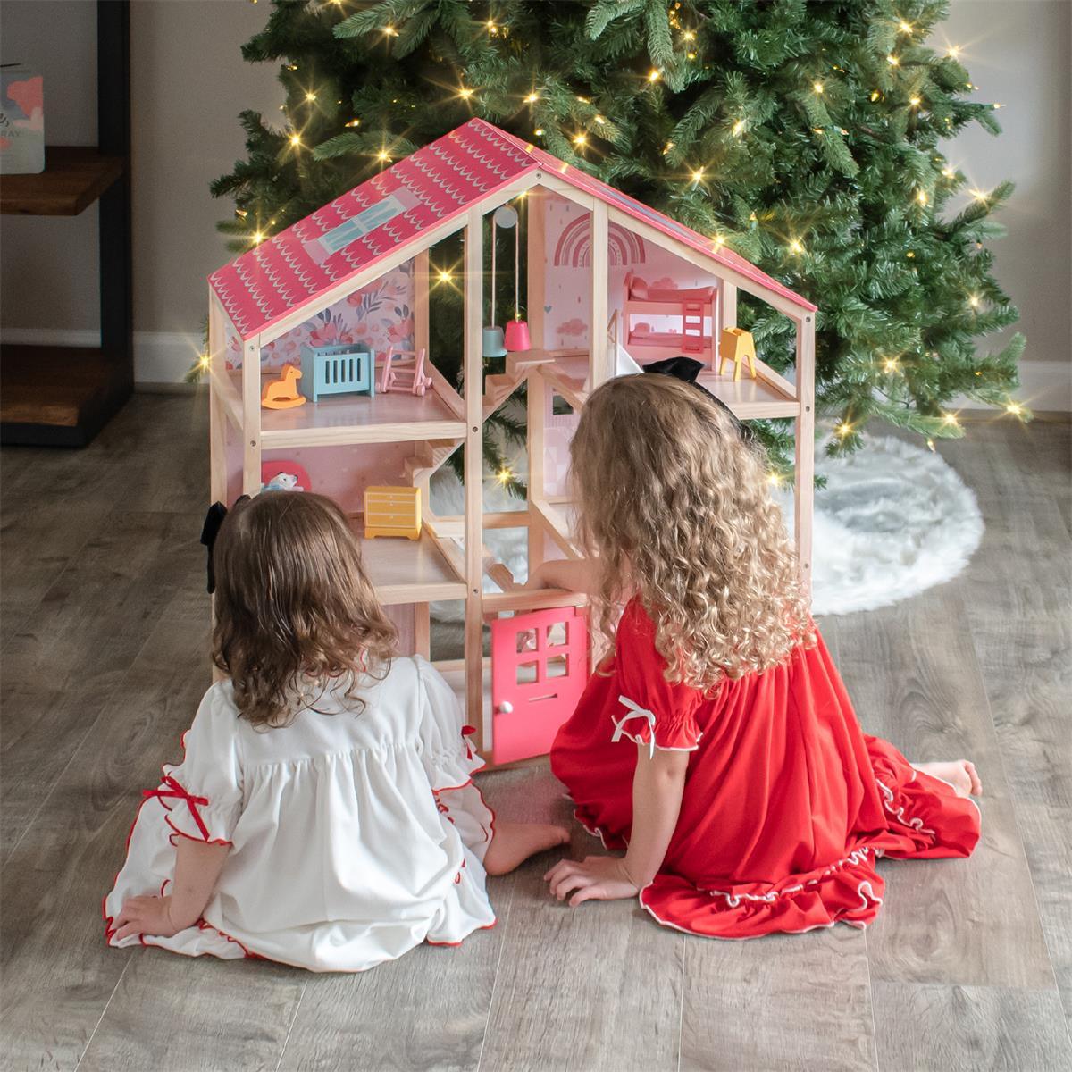 Two young children in festive pajamas sit by a decorated Christmas tree, playing with the Tiny Land Sweet Dreams Playset—Pink Dollhouse + Pink-White Playhouse. The curly-haired kids are seen from behind, enjoying the colorful set.|pink