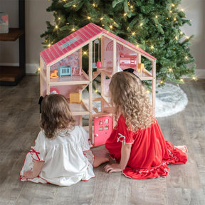 Two young children in festive pajamas sit by a decorated Christmas tree, playing with the Tiny Land Sweet Dreams Playset—Pink Dollhouse + Pink-White Playhouse. The curly-haired kids are seen from behind, enjoying the colorful set.|pink