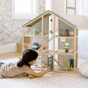 A young child plays on the floor, arranging miniature furniture in the Tiny Land® Sweetwood Evergreen Dollhouse without Dolls by Tiny Land. The room features light-colored walls and a patterned rug.|green