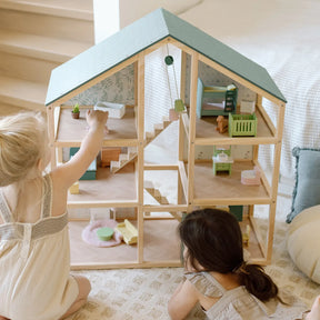 Two young children play with the Tiny Land Little Green World Gift Set, arranging furniture and figures in the Sage Dollhouse while the Sage Storage Kitchen adds to their imaginative fun on the rug by the staircase.|green