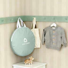 A soft green round bag labeled Tiny Land, a beige tote, and a gray knit sweater hang above a white shelf with a ceramic cow—charming decor for cozy indoor adventures with the Tiny Land® Tiny Sprout Castle Tent.|Green