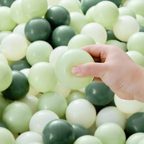 A hand holds a pale green Tiny Land® Ocean Ball from the 200-piece assorted set by Tiny Land, above a pile of similar non-toxic play balls in light green, white, and dark green—perfect for ball pits.|Green