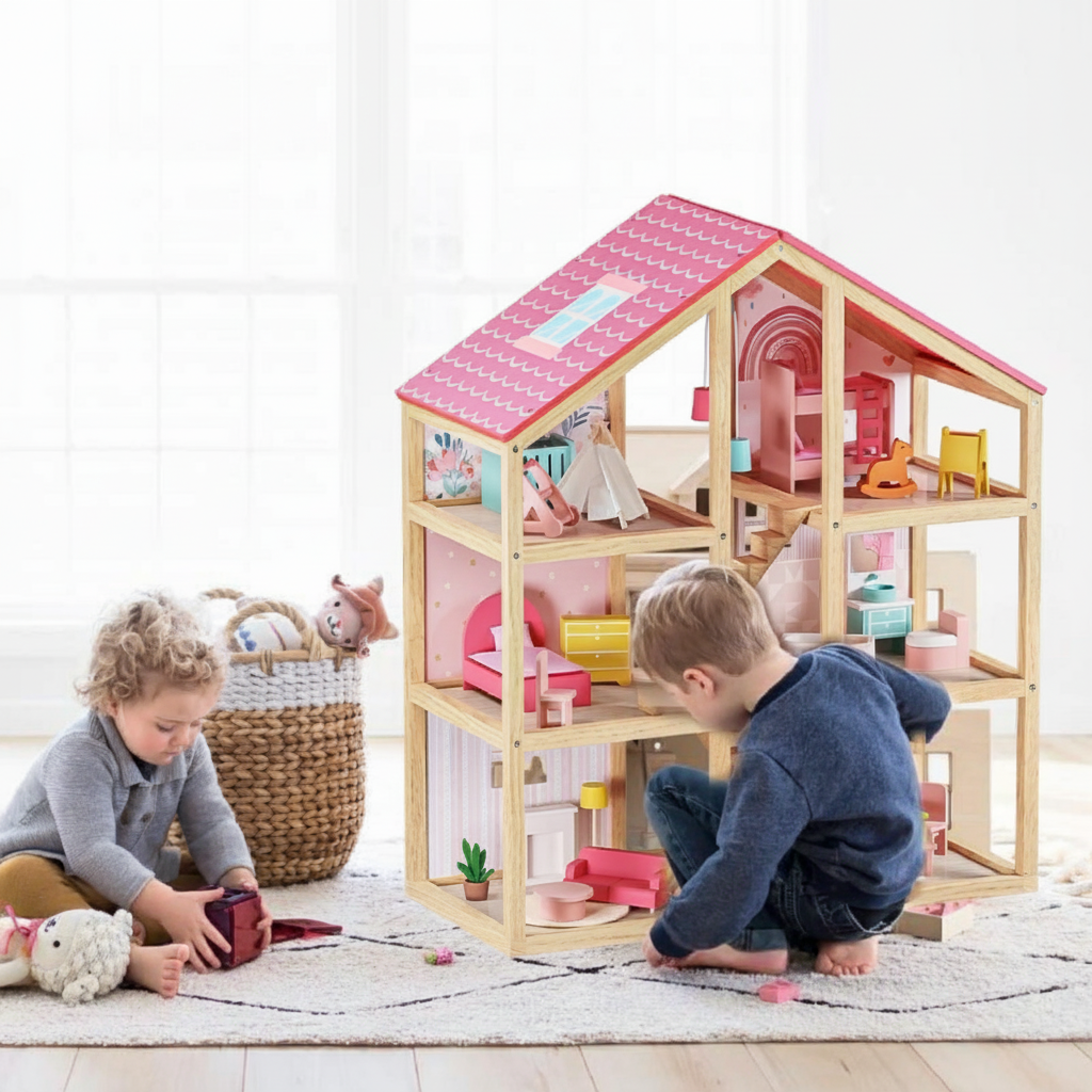 Two young children play on a rug with the Tiny Land Sweet Dreams Playset—a pink dollhouse and pink-white playhouse for girls, complete with colorful furniture. A basket of stuffed animals sits in the background.|pink
