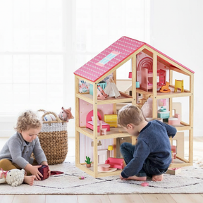 Two young children play on a rug with the Tiny Land Sweet Dreams Playset—a pink dollhouse and pink-white playhouse for girls, complete with colorful furniture. A basket of stuffed animals sits in the background.|pink