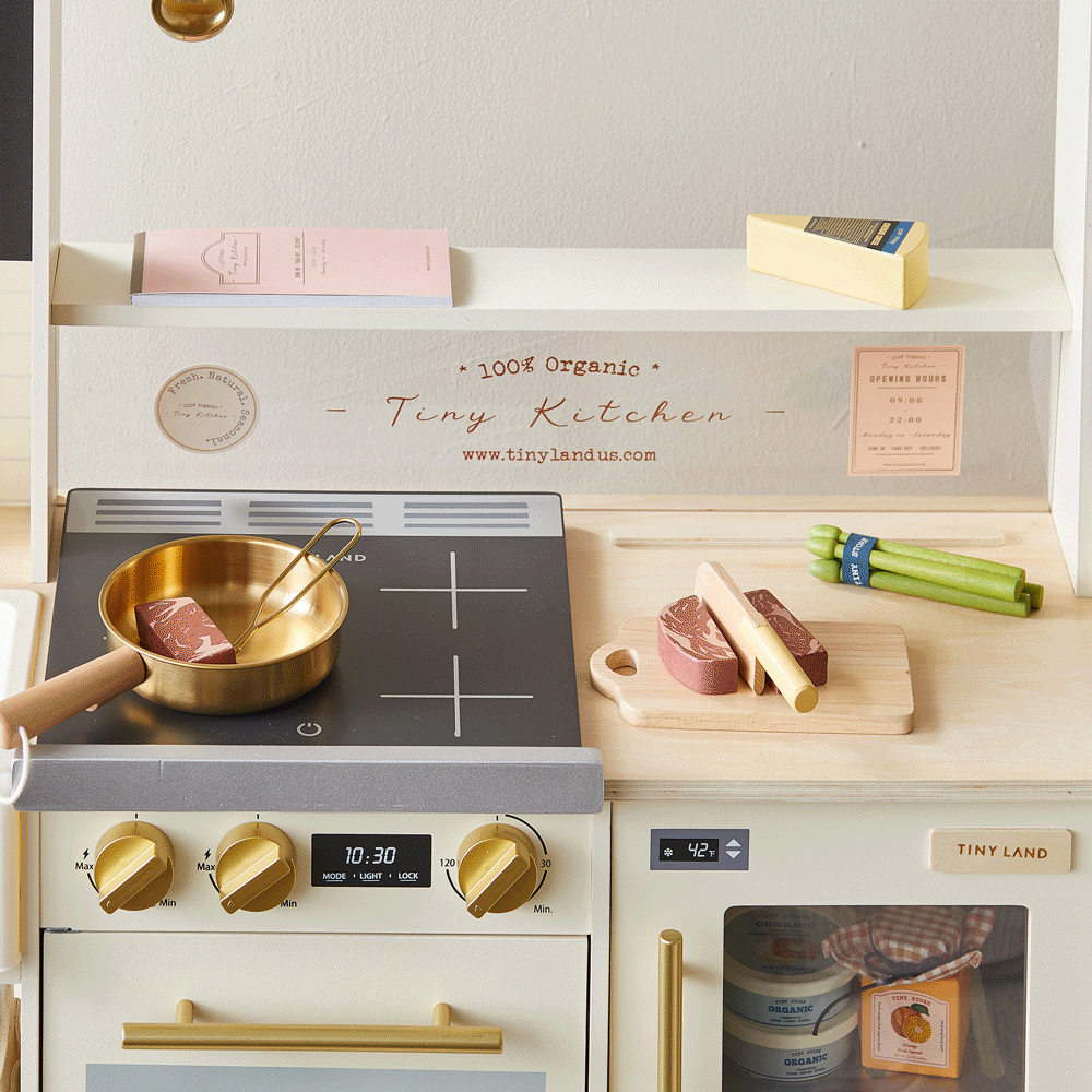 The Tiny Land® BistroSwitch Kitchen & Fridge Set by Tiny Land is a miniature play kitchen for kids, featuring a stovetop, pan, cutting board, toy food items, and small kitchen accessories neatly arranged on light-colored shelves and counters.