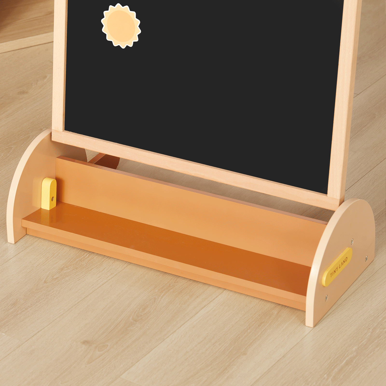 The Tiny Land® Double-Sided Arched Magnet Chalkboard & Art Kit by Tiny Land features a wooden frame with both a chalkboard and magnetic surface, a playful yellow sun-shaped magnet, and a convenient tray at the bottom. Placed on a light wooden floor, this art easel is an ideal addition to any kids’ art accessory kit.