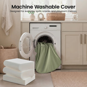 A green fabric cover of the Tiny Land® GentleSnug Kid Chair is partially inside a front-loading washing machine in a laundry room. Text above reads, “Machine Washable Cover.” Designed for everyday spills, snacks, and playroom messes, the foldable kids’ chair from Tiny Land is perfect for any toddler couch or playroom furniture setup.|Sage