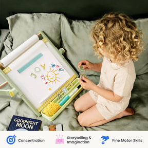 A young child sits by the Tiny Land® Double-Sided Magnetic Tabletop Easel, arranging magnetic letters and drawings that spell JOY alongside a sun illustration. Beside the Tiny Land kids’ easel, a copy of Goodnight Moon and educational icons are visible in the scene.|Green