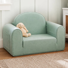 The Tiny Land® GentleSnug Kids Sofa Chair by Tiny Land, in light green with wide arms and a side pocket, sits on a wooden floor; a beige stuffed bunny rests on the left side of the toddler chair.