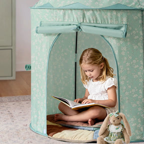 A young girl sits cross-legged inside the light blue Tiny Land® Compact Adventure 3-in-1 Play Tunnel, reading a book. A stuffed bunny in a dress rests on a quilted mat beside her. The cozy scene radiates calm, while the attached tunnel from Tiny Land hints at nearby adventures waiting to be discovered.|green