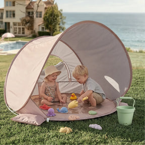 Two young children play with toy sea animals and a yellow rubber duck in the Tiny Land® 3-in-1 Baby Beach Tent by Tiny Land, set up near a house and pool, surrounded by green grass and trees.