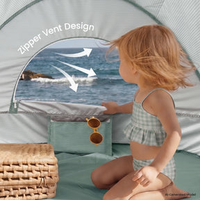 A young child in a checkered swimsuit sits inside the Tiny Land® Baby Beach Tent & Sand Toy Set by Tiny Land, gazing through the tent’s zippered vent. Nearby are sunglasses and woven baskets. White arrows draw attention to the innovative Zipper Vent Design.|Green