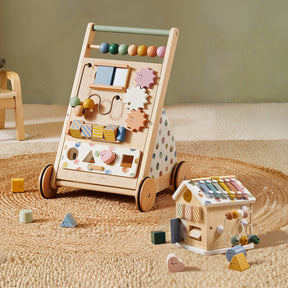 The Tiny Land Complete Development Playset — Baby Walker + Activity Cube rests on a woven rug beside scattered colorful blocks in a cozy playroom, creating an inviting space that fosters fine motor skill development through engaging activities and thoughtful design.