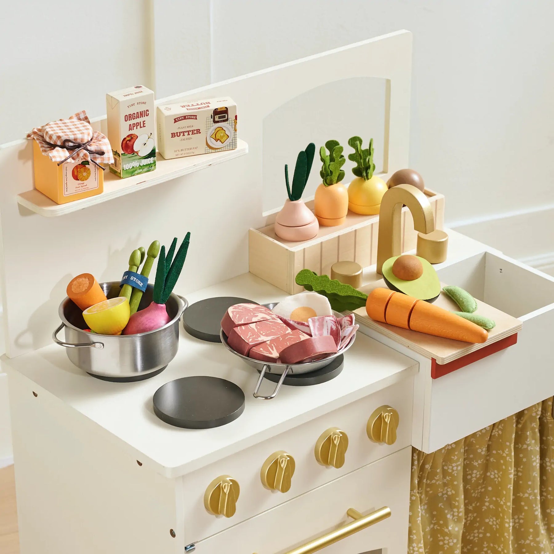 A toy kitchen set featuring the Tiny Land® Organic Dairy Pack by Tiny Land Play Food, with realistic play food for toddlers displayed on a white play stove with gold knobs and a yellow patterned curtain.