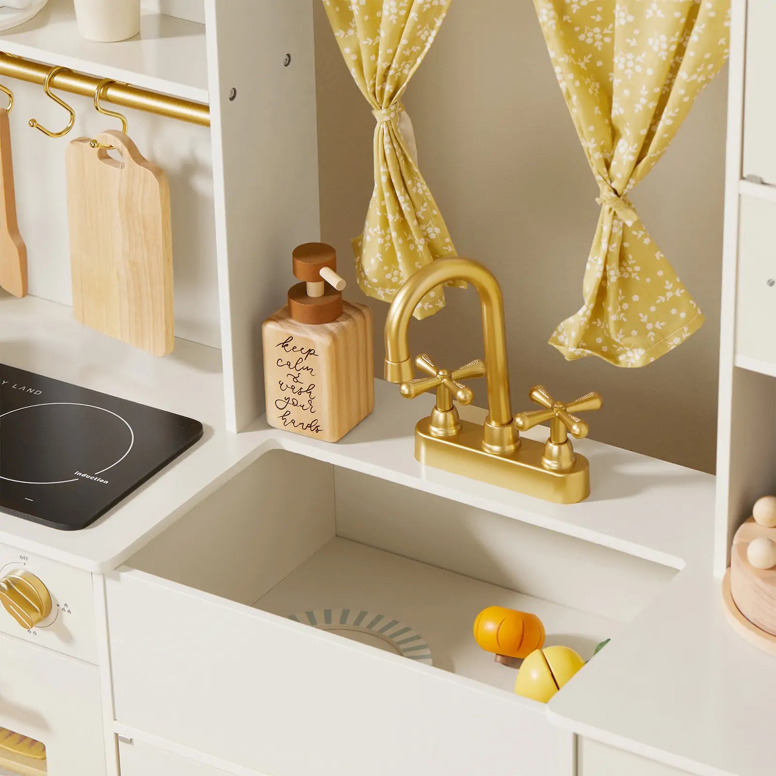 The Tiny Land® Iconic Wooden Play Kitchen—Cream Pretend Cooking Set for Kids features a gold faucet, yellow floral curtains, soap dispenser, wooden utensils, stovetop, and play food like sliced lemon and orange for endless imaginative play.