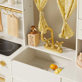 The Tiny Land® Iconic Wooden Play Kitchen—Cream Pretend Cooking Set for Kids features a gold faucet, yellow floral curtains, soap dispenser, wooden utensils, stovetop, and play food like sliced lemon and orange for endless imaginative play.